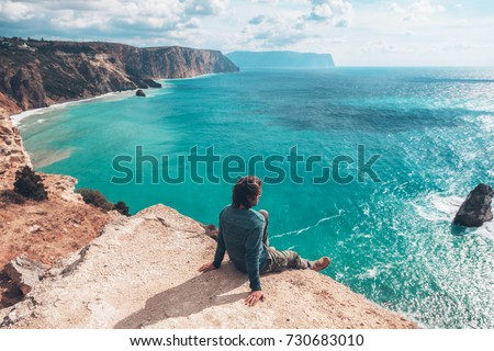 Man traveler sitting on mountain alone and looking at autumn sea landscape. Hiking in cold season. Wanderlust concept scene.