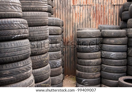 Car tyres stacked in a tyre distribution centre in front of old corrugated steel