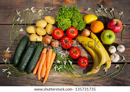 Sunlit selection of fresh vegetables and fruit framed with Snowdrop flowers on a wooden table