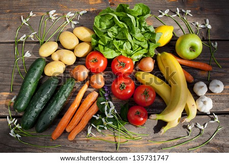 Sunlit selection of fresh vegetables and fruit framed with Snowdrop flowers on a wooden table