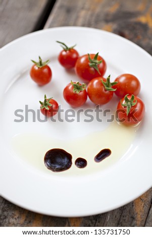 Cherry tomatoes with olive oil and balsamic vinegar on a white plate, focus on foreground.
