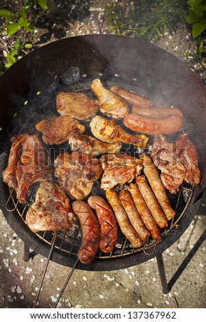 variety of meat on an outdoor, sunlit, smoking barbecue grill