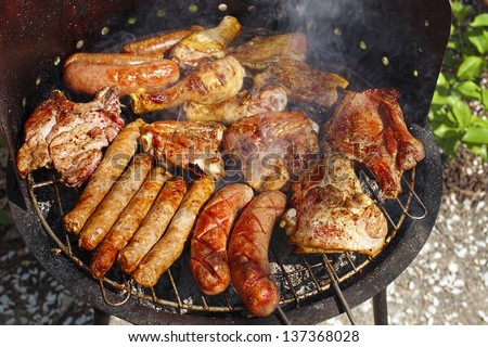 variety of meat on an outdoor, sunlit, smoking barbecue grill