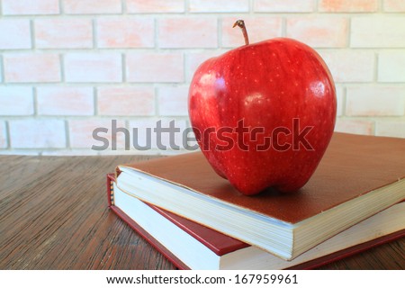 A school teacher's desk with stack of exercise books and apple . A blank blackboard in soft focus background provides copy space.