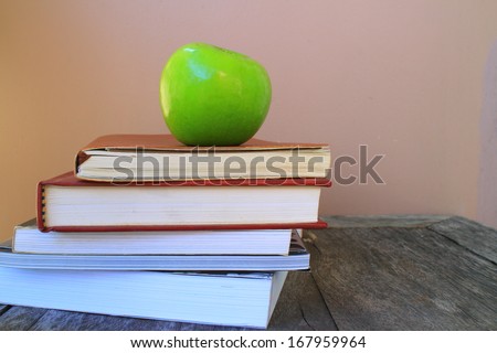 A school teacher's desk with stack of exercise books and apple . A blank blackboard in soft focus background provides copy space.