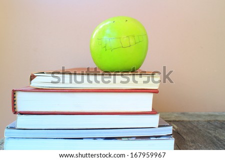 A school teacher\'s desk with stack of exercise books and apple . A blank blackboard in soft focus background provides copy space.