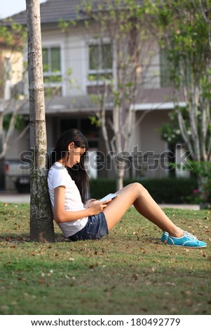 Tablet computer. Relaxed young  teenage in garden smiling content, happy and reading on tablet pc at home in garden. Lifestyle image of beautiful mixed Asian Caucasian girl relaxing smiling happy