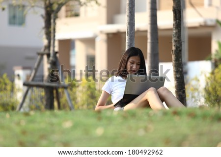 note book computer. Relaxed young  teenage in garden smiling content, happy and reading on tablet pc at home in garden. Lifestyle image of beautiful mixed Asian Caucasian girl relaxing smiling happy