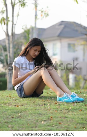 Tablet computer. Relaxed young teenage in garden smiling content, happy and reading on tablet pc at home in garden. Lifestyle image of beautiful mixed Asian Caucasian girl relaxing smiling happy