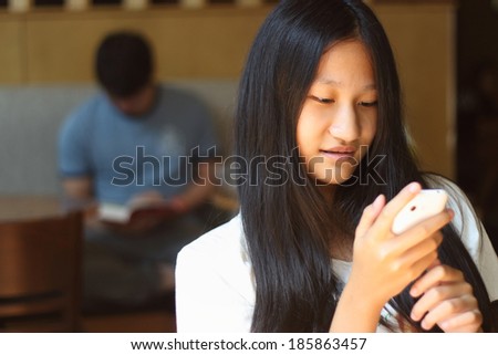 Cafe city lifestyle woman on phone drinking coffee texting text message on smartphone app sitting indoor in trendy urban cafe. Cool young modern mixed race Asian Caucasian female model in her 15s.