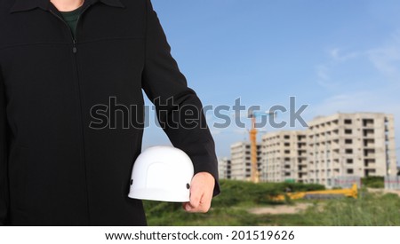 engineer holding white helmet for workers security on background of new highrise apartment buildings and construction cranes