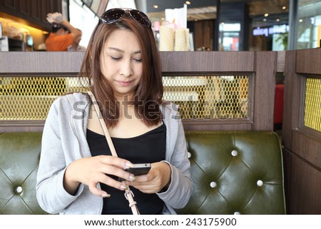 Cafe city lifestyle woman on phone drinking coffee texting text message on smartphone app sitting indoor in trendy urban cafe. Cool young modern mixed race Asian Caucasian female model in her 40s.