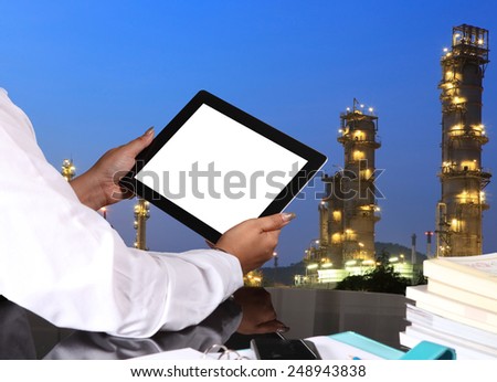 tablet pc in hand  on office table with oil refinery background