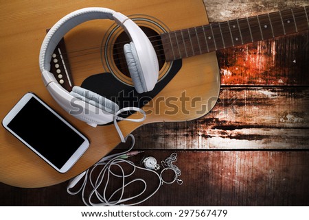 Acoustic guitar ,cell phone and headphone on old wooden table