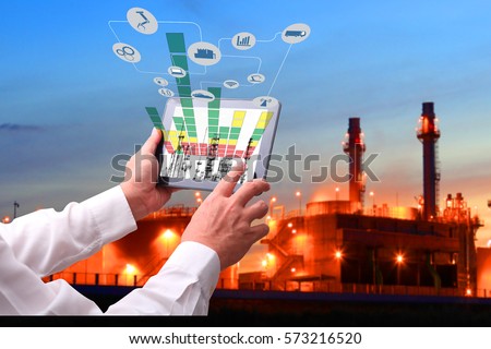Industry 4.0 concept .Man hand holding tablet with Augmented reality screen and automate wireless Robot arm software at industrial room in smart factory.Window showing oil refinery industry background