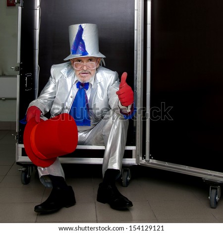 Magician in a white suit with hat sitting in a box before the show