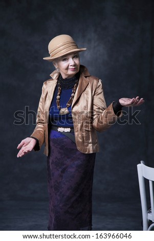 beautiful elderly woman in hat gesturing with hands on a dark background