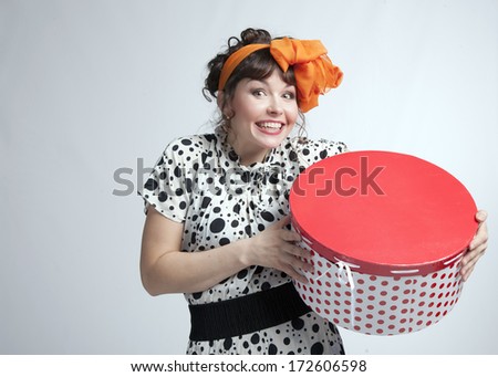 Young happy girl in a polka dot dress and bow on her head holding red gift box on a gray background