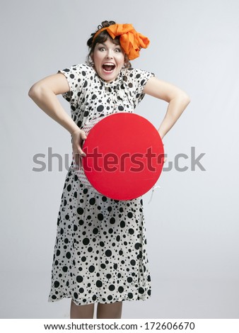 Young happy girl in a polka dot dress and bow on her head holding red gift box on a gray background