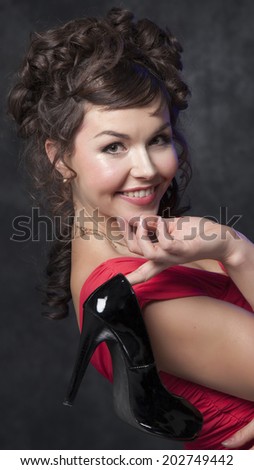 young beautiful woman posing with shoes in red dress on black background
