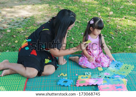 Mother teaching her daughter to learn by playing alphabet jigsaw