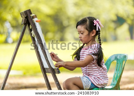Little Asian girl painting on easel
