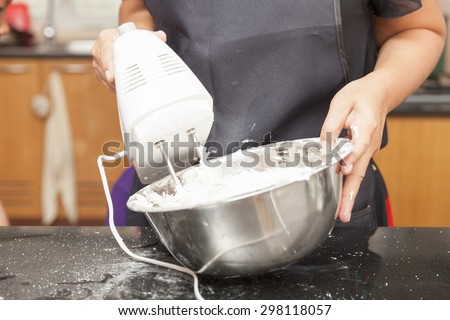 Mother using electric mixer to mix ingredients of sponge cake