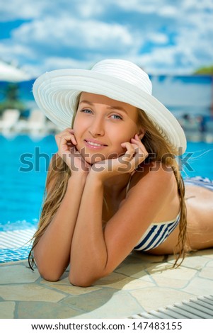 Smiling beautiful woman in hat relaxing at the pool