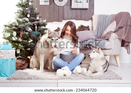 young beautiful brunette woman with a gift in a box and  husky dogs in a Christmas setting