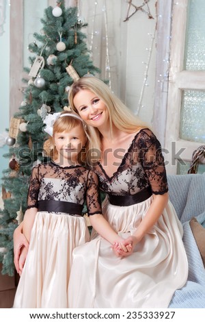 Young beautiful woman with her daughter in a Christmas setting. The same dress.