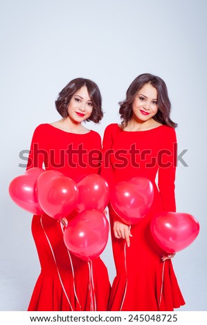 Two beautiful young woman in a long red dress with balloons in the form of heart in his hands. Valentine\'s Day. Twins.