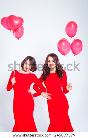 Two young beautiful women in a long red dress with balloons in the form of heart in his hands. Twins.