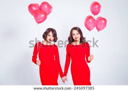 Two young beautiful women in a long red dress with balloons in the form of heart in his hands. Twins.