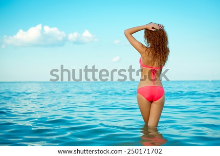 Young beautiful sexy woman in a swimsuit standing back in the water of the sea. Model.