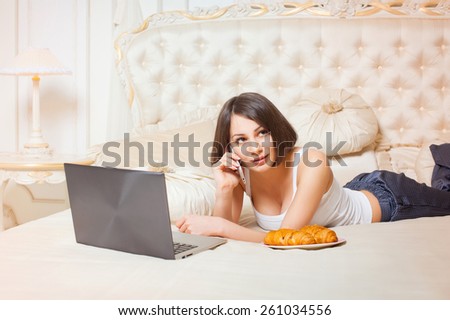 Young beautiful woman lying on the couch with a laptop and talking on the phone.