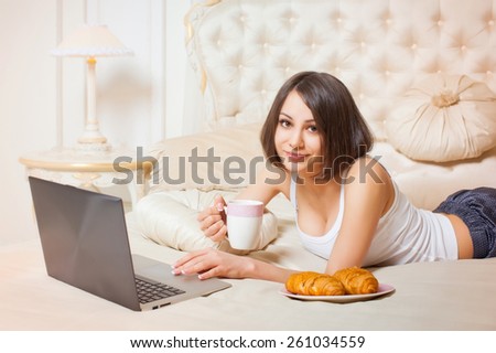 Young beautiful woman lying on the couch with a laptop and a cup of coffee in his hands.