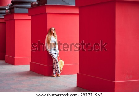 Young beautiful blonde woman on a city street .Model .Fashion. Red background.