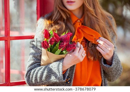 Detail of a beautiful young fashion woman wearing coat with a bouquet of tulips in the city streets . Street style .