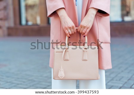 Fashionable beautiful woman with handbag in pink coat, white overalls and blue shoes on the city streets.