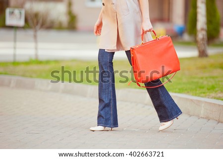 Stylish young woman in a beige trench, jeans flared and high-heeled shoes on the streets. Fashion.