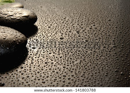 massage stones surrounded by water drops on a black background