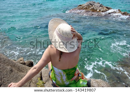 woman sitting on sea rocks looking at the horizon with his hat
