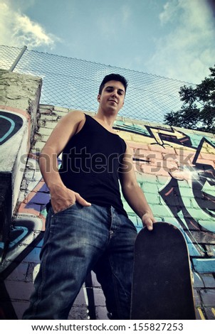 young man posing with his skateboard on a wall with graffiti