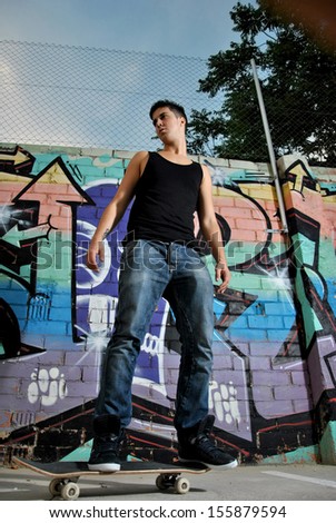 young man posing with his skateboard on a wall with graffiti