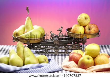 Apples and pears on an old balance. The balance is located on a black-white checkered tablecloth.