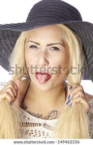 A naughty woman with very fair hair wear summer clothes and a black hat stick out her tongue. The person is exempted on white background.