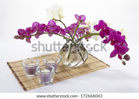 A bouquet of white and purple orchids in a vase. The vase is standing on a place mat made of bamboo.