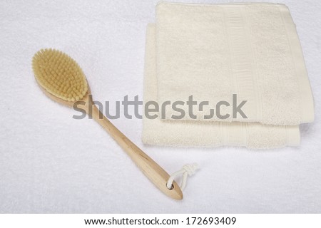 A bath brush is laying beneath two folded, naturally colored towels.