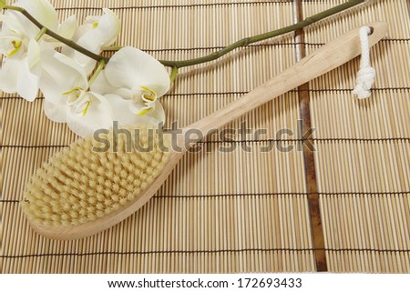A bath brush is laying on a mat of bamboo. The decoration is made of a white orchid.