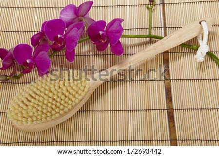 A bath brush is laying on a mat of bamboo. The decoration is made of a purple orchid.